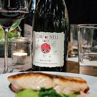 Rødvin på et dækket bord bag en tallerken med fisk