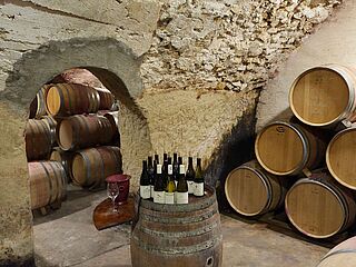 Weinflaschen stehen auf einem Fass in einem Kellergewölbe