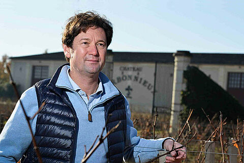 Winzer auf dem Weingut Carbonnieux, Haus im Hintergrund, blauer Himmel