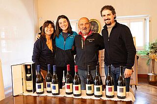 Winzer stehen hinter einem Tisch davor stehen ein paar Flaschen Wein
