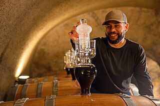 Mann mit Capi nimmt eine Weinprobe aus dem Weinfass im Weinkeller Eisele Vineyard Mann mit Capi nimmt eine Weinprobe aus dem Weinfass im Weinkeller Eisele Vineyard