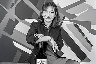 Magali Malet sitzt vor einem Bild mit einer Weinflasche