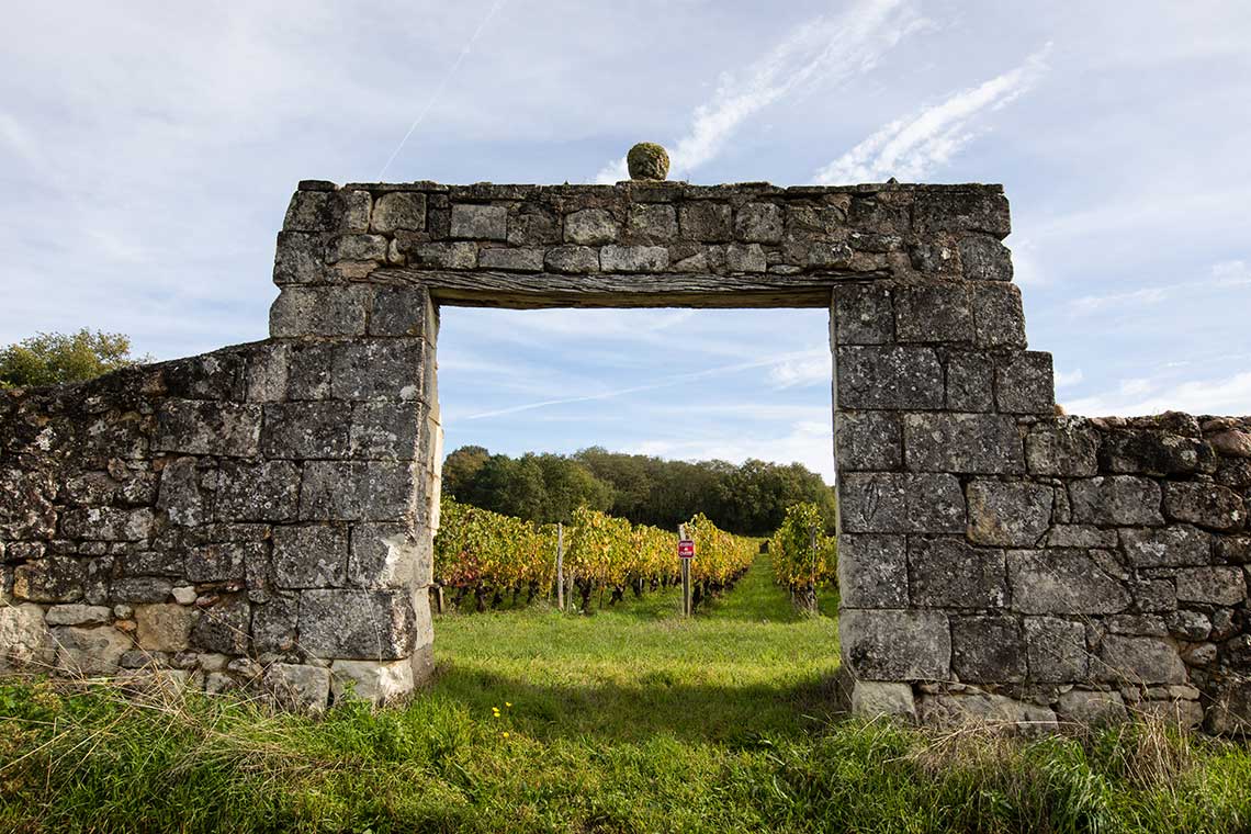 Steinmauer und Steinbogen vor einem Weinfeld, Weingut